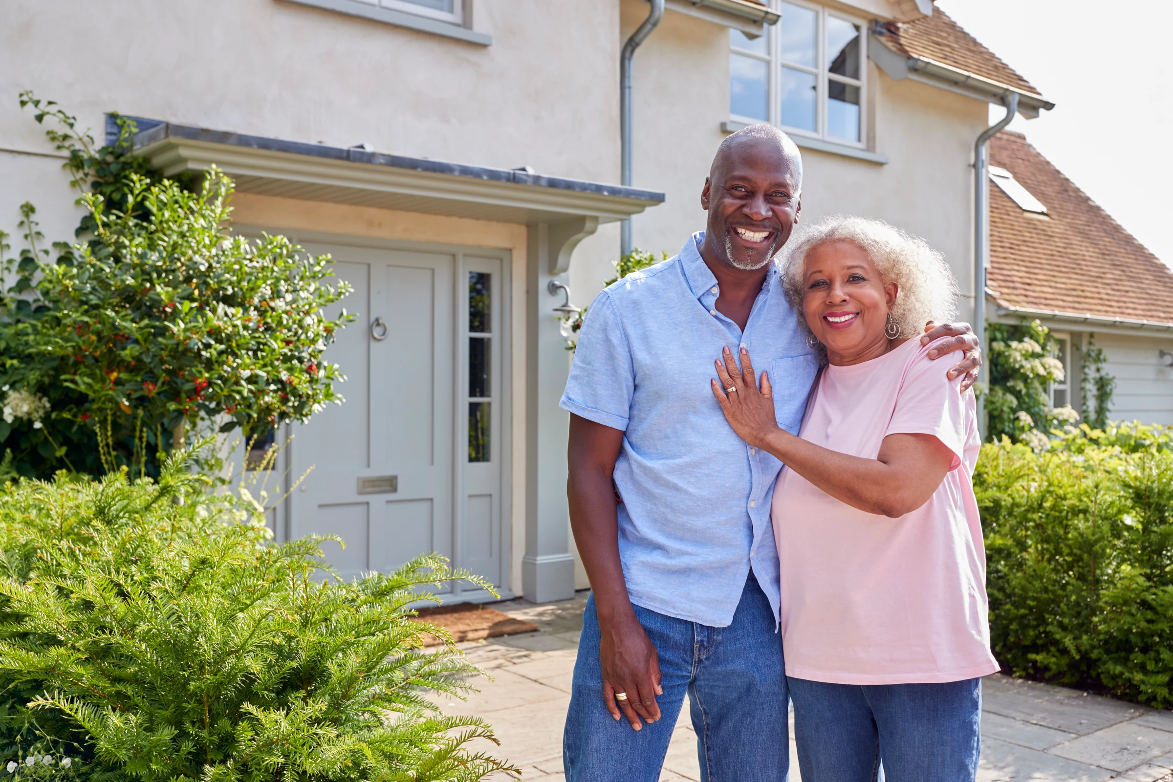 A smiling senior couple embracing in front of their home